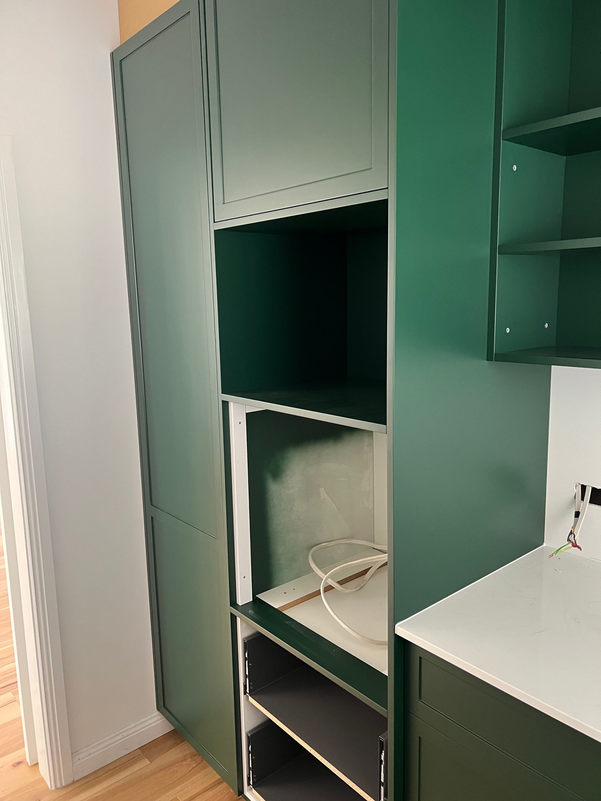 Green built-in cabinets with open compartments and shelves. A wire hangs in one of the open spaces.