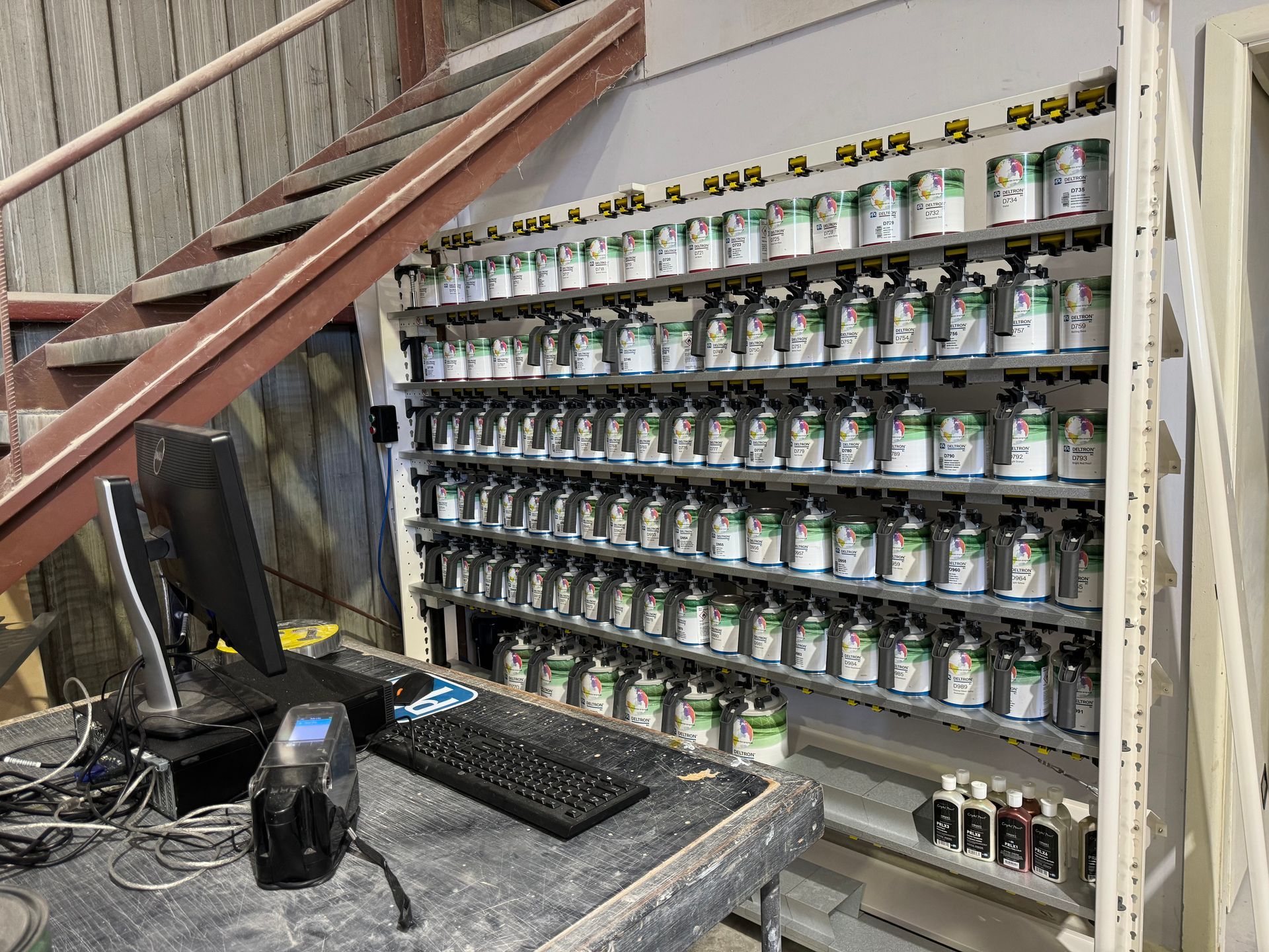 A paint mixing station with rows of paint cans, a computer, and a staircase.