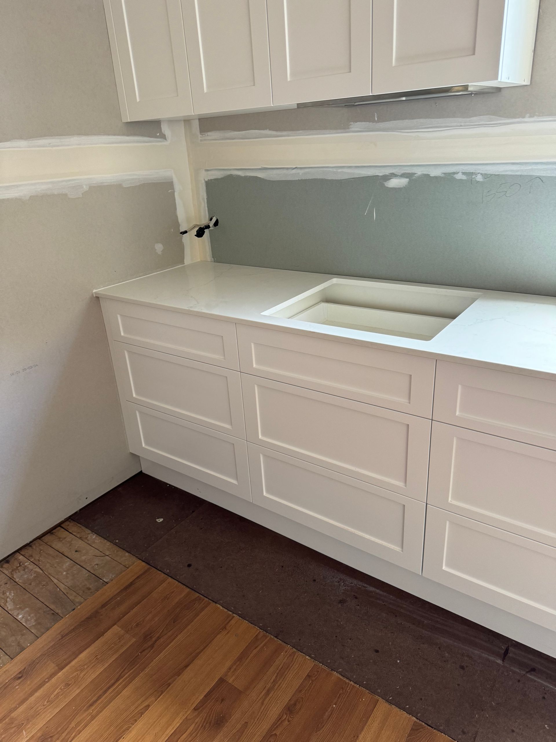 White kitchen cabinets and countertop installed. Gray walls and wood flooring are also visible.