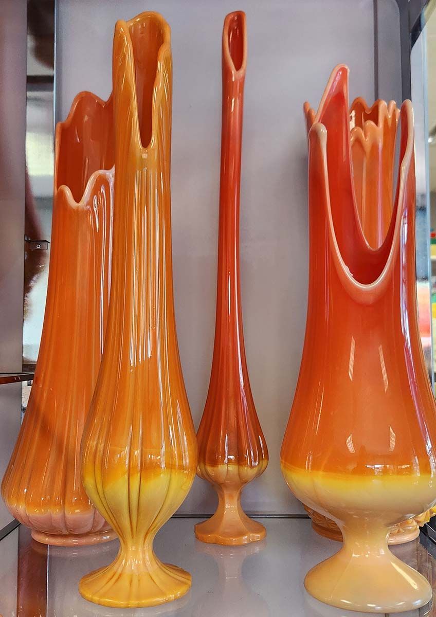 A display of orange and yellow vases on a glass shelf