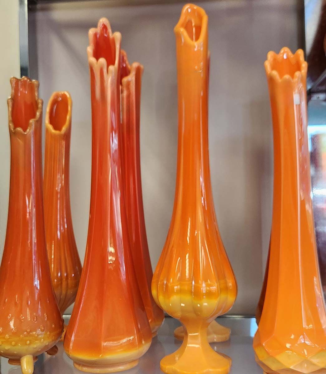 A row of orange vases are lined up on a shelf