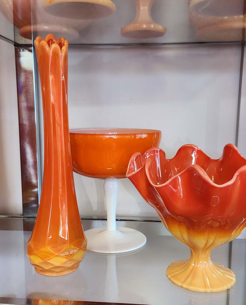 A glass shelf with three vases and a bowl on it