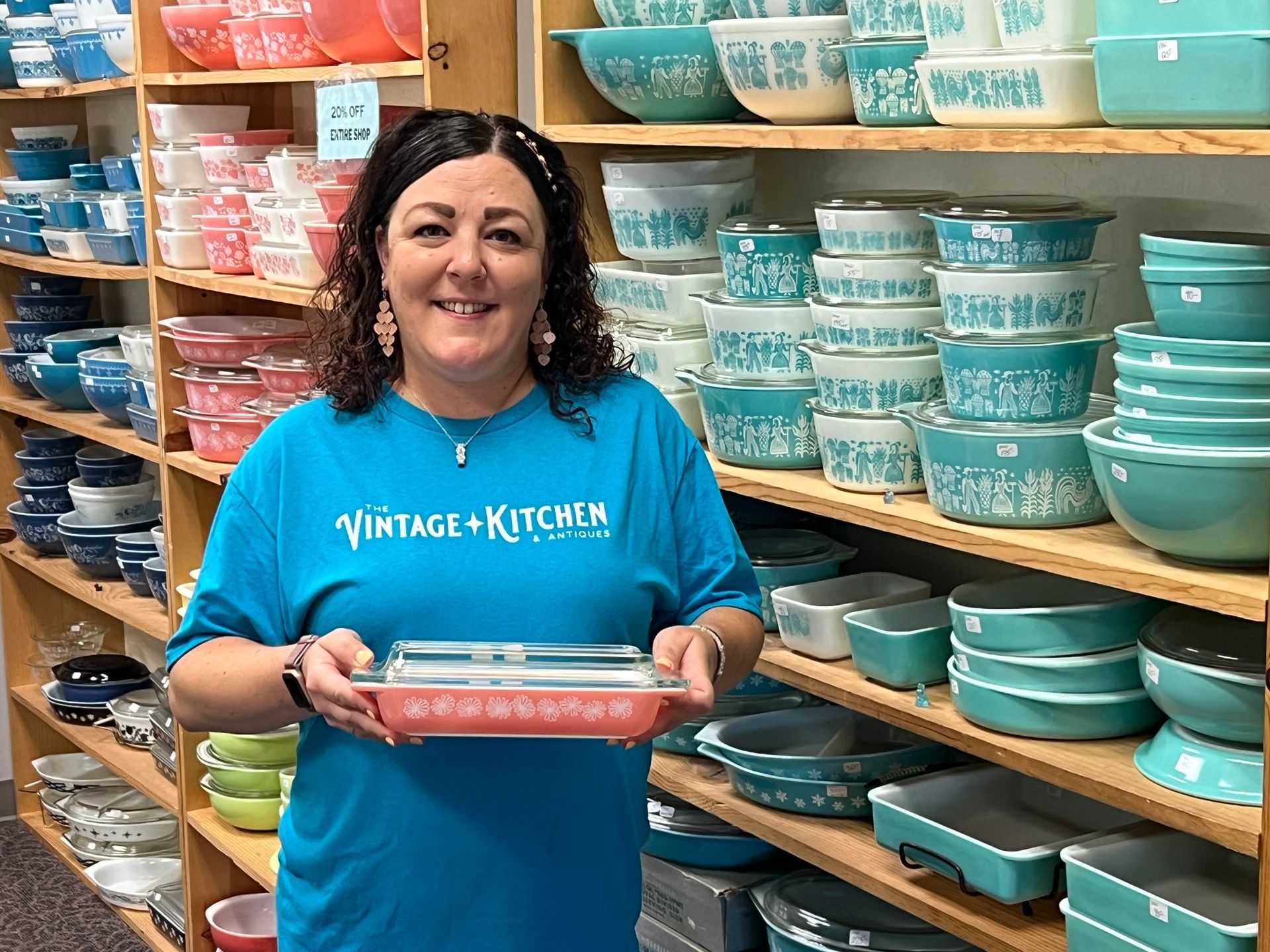 A woman wearing a vintage kitchen shirt is holding a casserole dish
