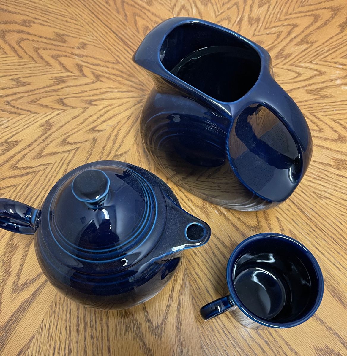 A blue teapot a pitcher and a cup on a wooden table