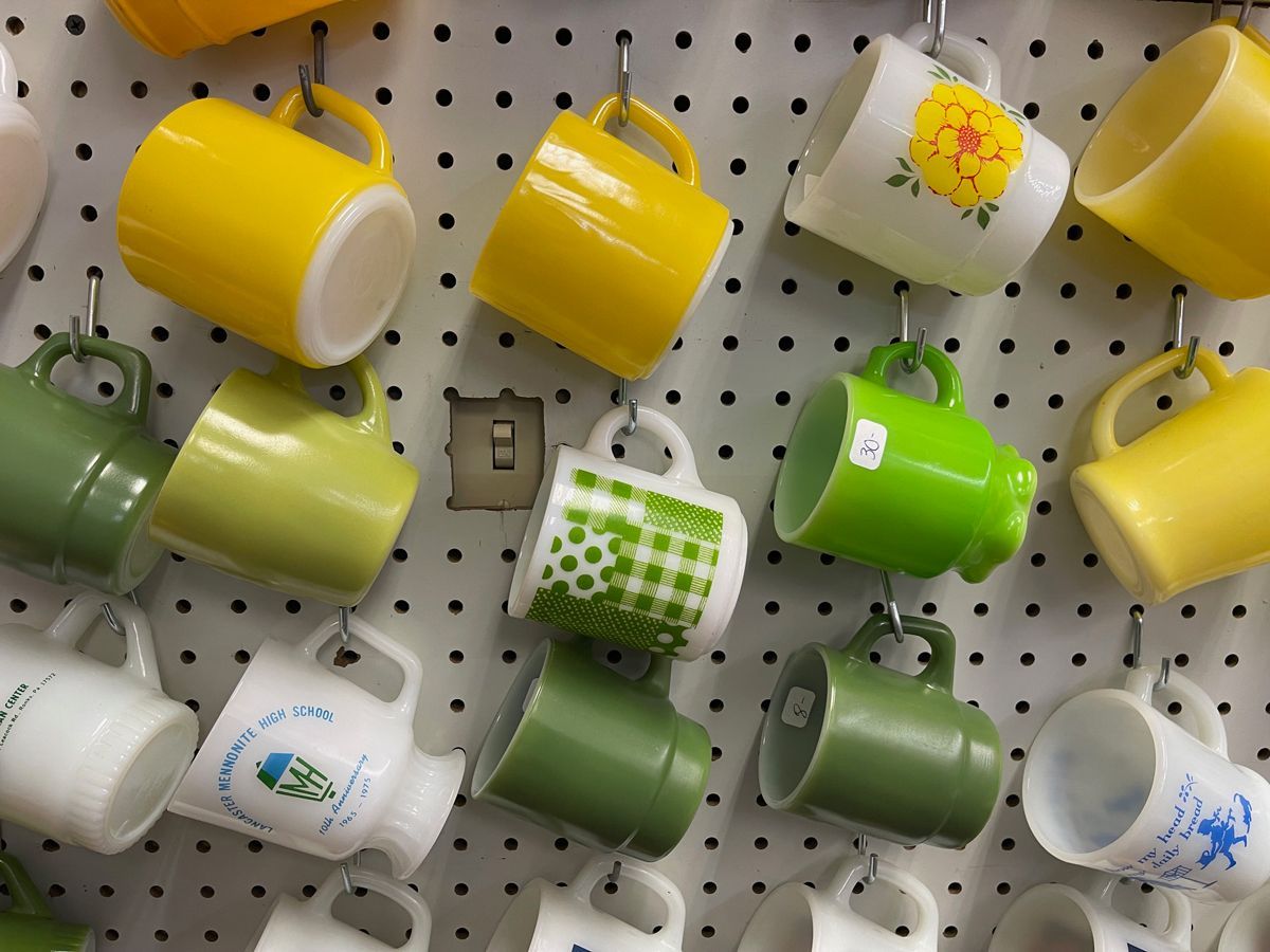 A bunch of different colored coffee mugs hanging on a wall