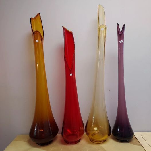 Five different colored glass vases are lined up on a table