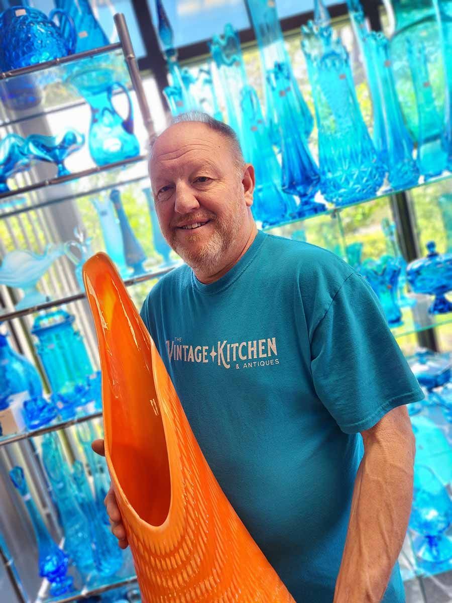 A man in a blue shirt is holding a large orange vase.