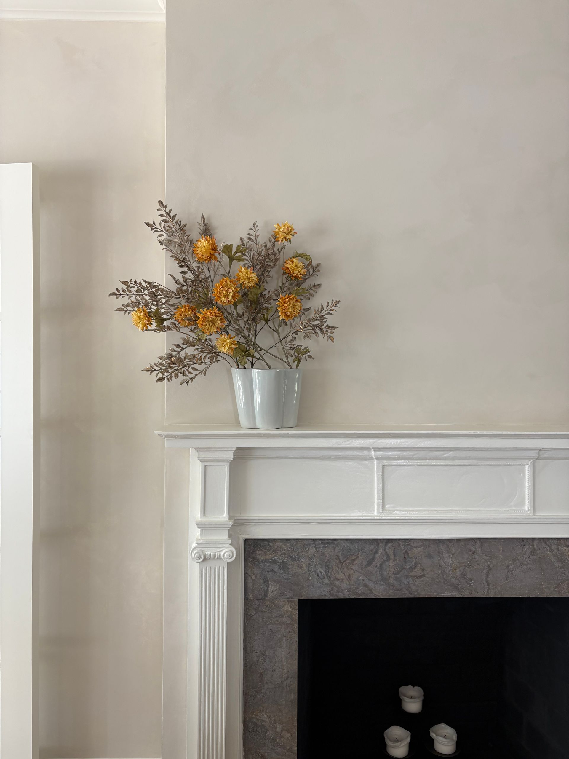 White mantel with ceramic vase, orange flowers, and small candles.