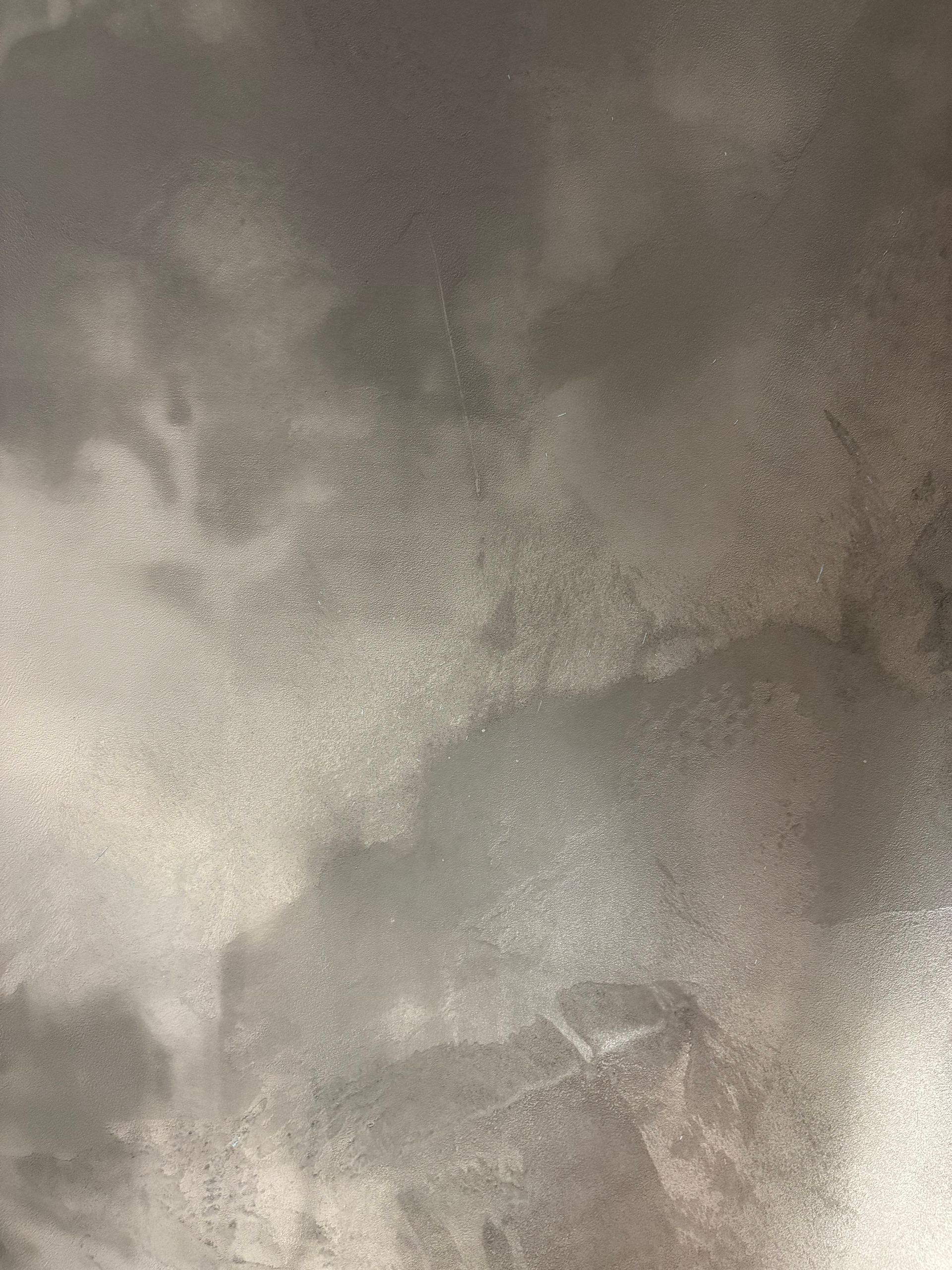 Abstract gray surface with cloudy textures and faint linear patterns, resembling plaster or concrete with soft tonal variation.