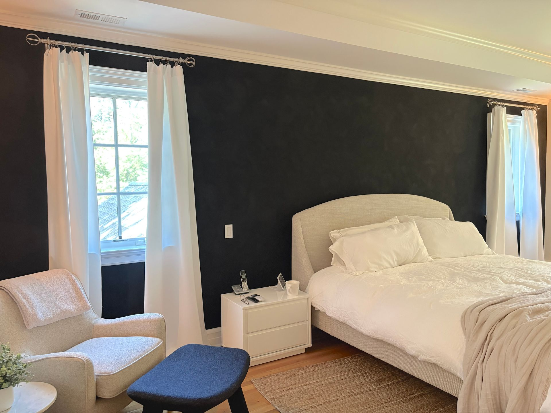 Bedroom with white bedding, dark wall, and cozy armchair.