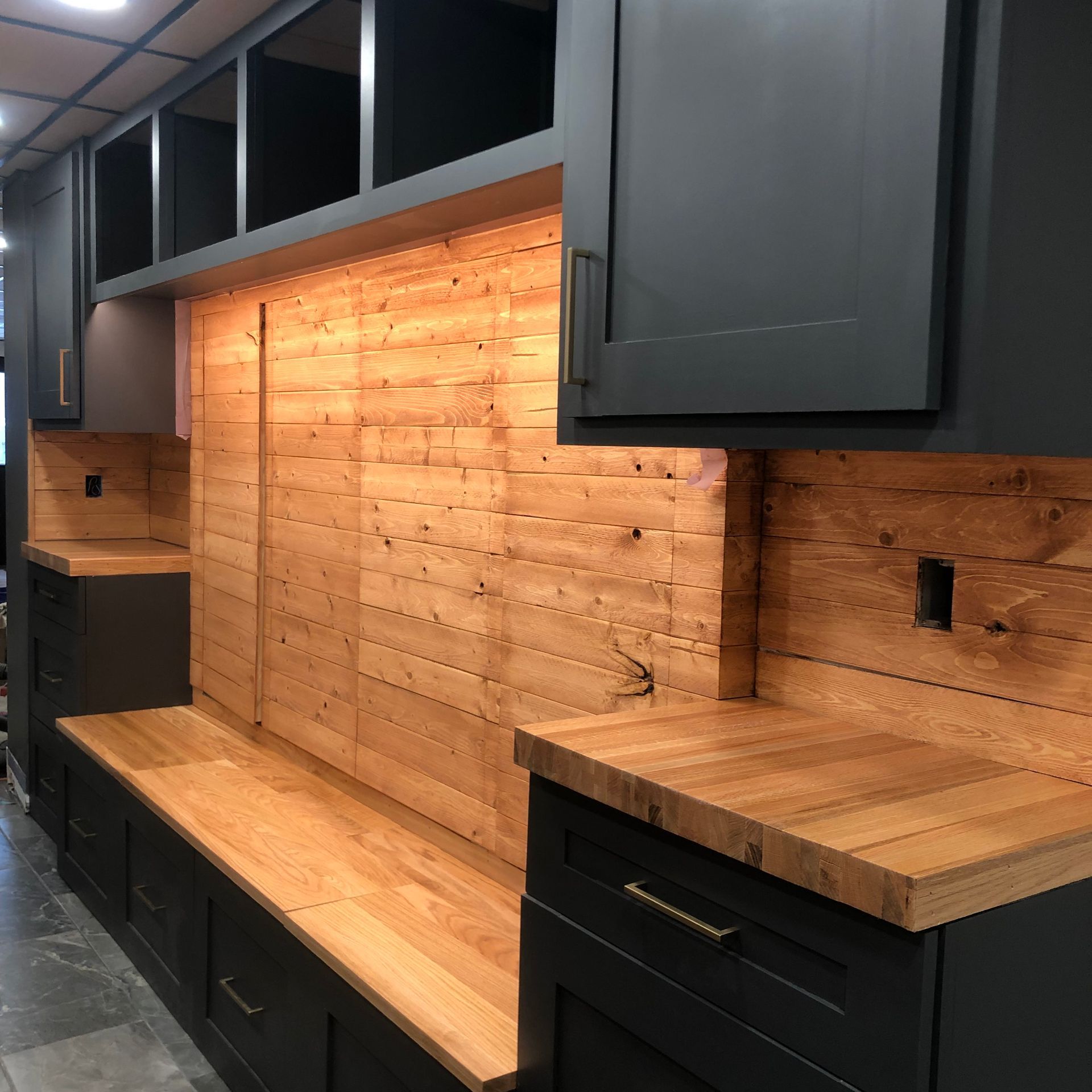 Contemporary kitchen with matte dark cabinets and natural wood countertops and backsplash, highlighted by under-cabinet lighting.