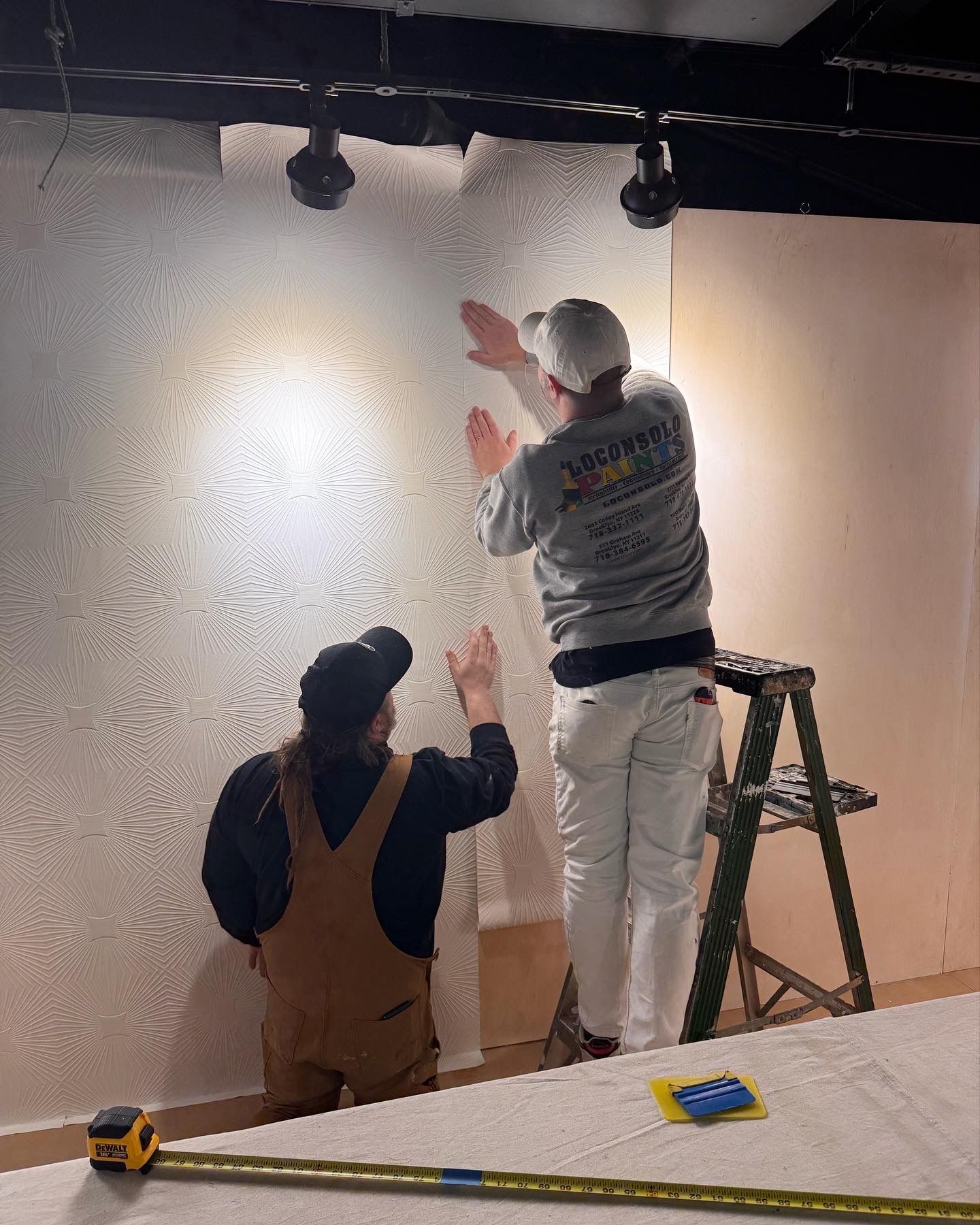 Wallpaper install: starburst texture applied with ladder and tools.