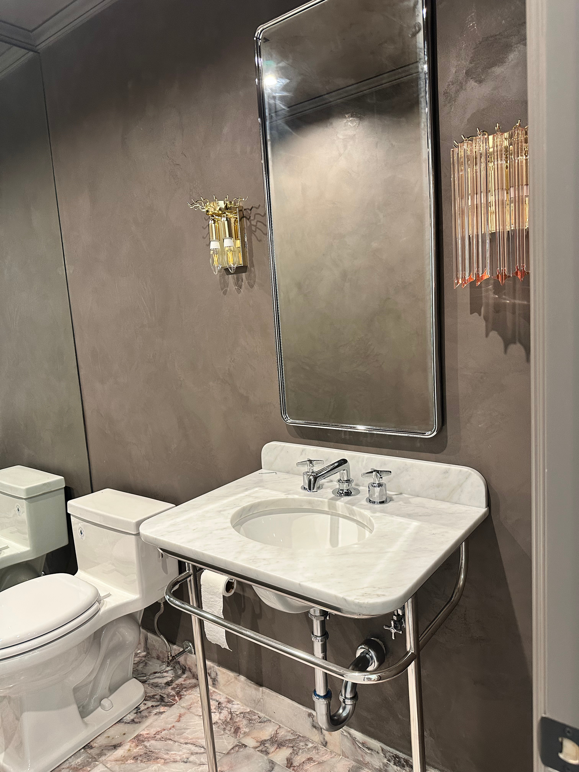 Bathroom with marble sink, chrome mirror, and warm lighting.