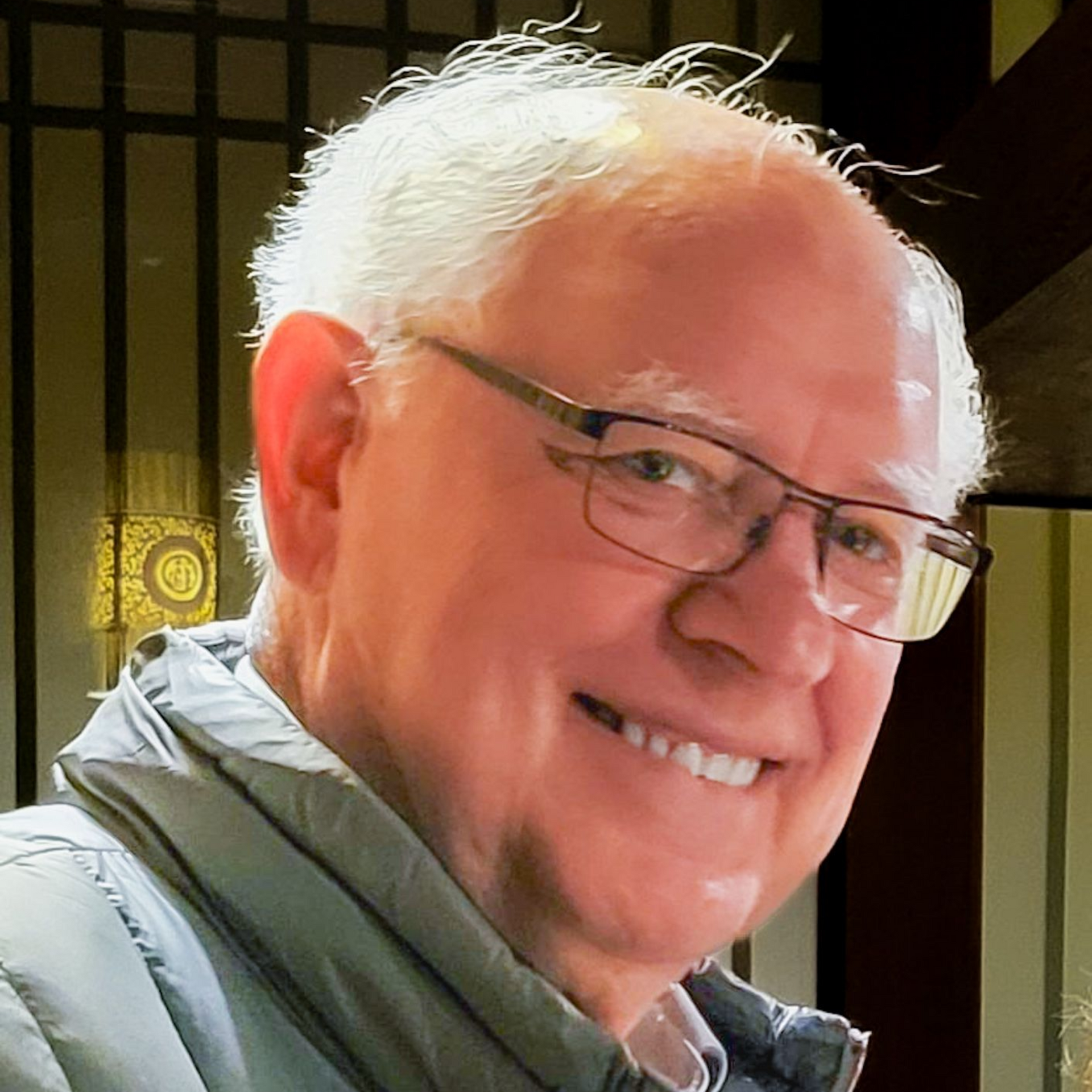 Smiling man with glasses in a gray jacket, indoors with warm light and a dark window background