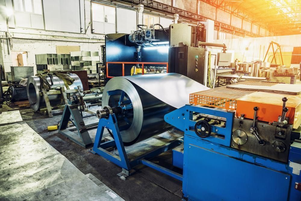 Coil Of Metal Sheet In A Blue Industrial Machine, Inside A Factory With Equipment — Sheetmetal Improvements & Design in Burleigh Heads, QLD