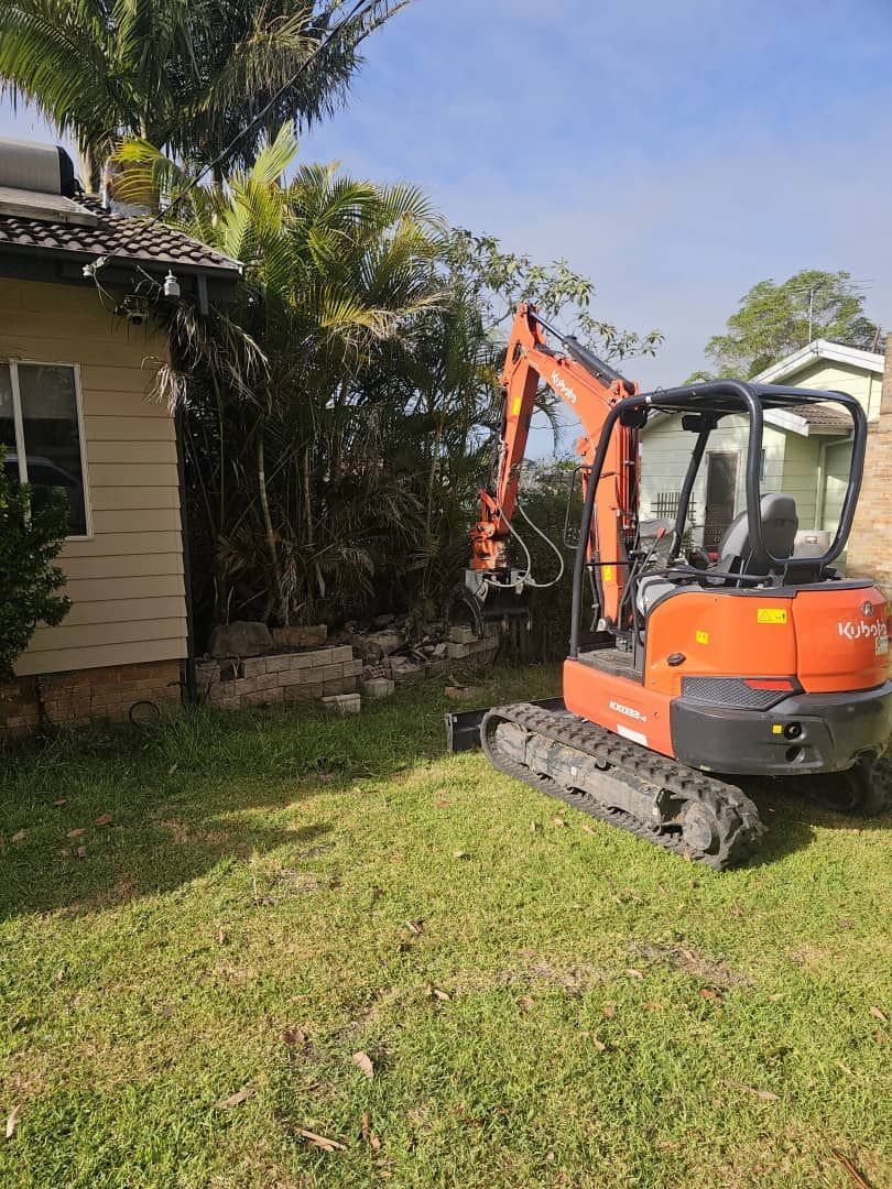 Orange Excavator Removing Foliage Next to a House With Beige Siding — JC Forestry in Paterson, NSW
