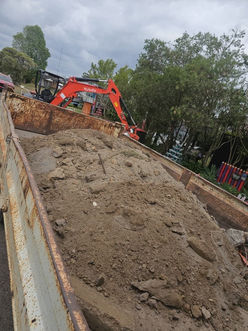 An Excavator Filling a Rusty Truck Bed With Dirt Under a Cloudy Sky — JC Forestry in Maitland, NSW