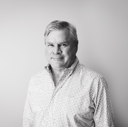 A man in a plaid shirt is standing in front of a white wall.