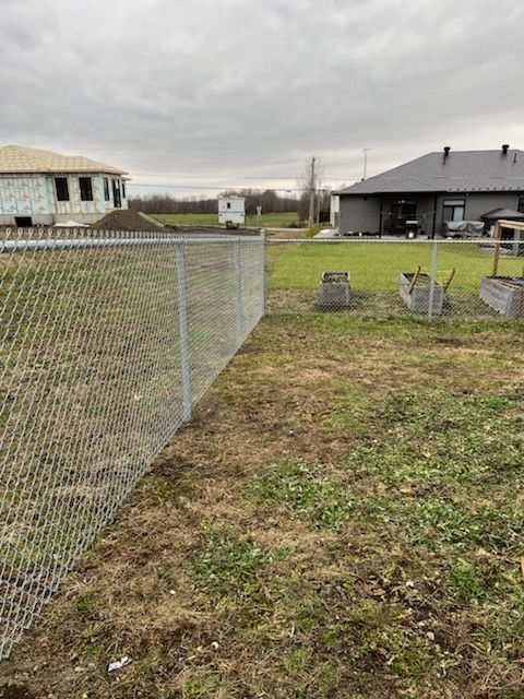 Clôture grillagée dans une cour, avec des maisons en arrière-plan sous un ciel couvert.