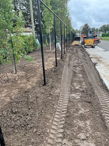 Clôture noire le long d'un chemin de terre, avec une chargeuse compacte et une bordure sur la droite.