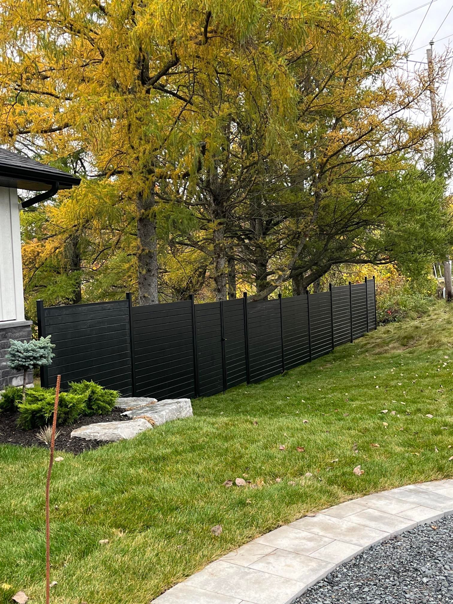 Clôture en treillis noir sur une colline verdoyante avec des arbres d'automne en arrière-plan.