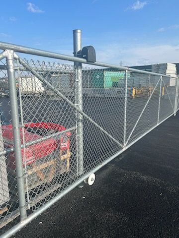 Clôture grillagée avec portail automatique, moteur et conteneur rouge; aménagement extérieur.