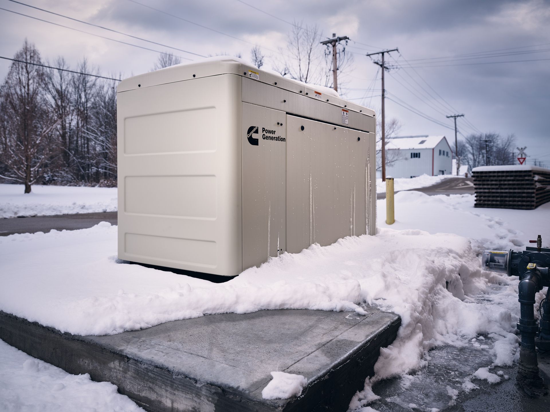 Générateur dans une zone industrielle enneigée avec des poteaux électriques, un bâtiment et des congères.