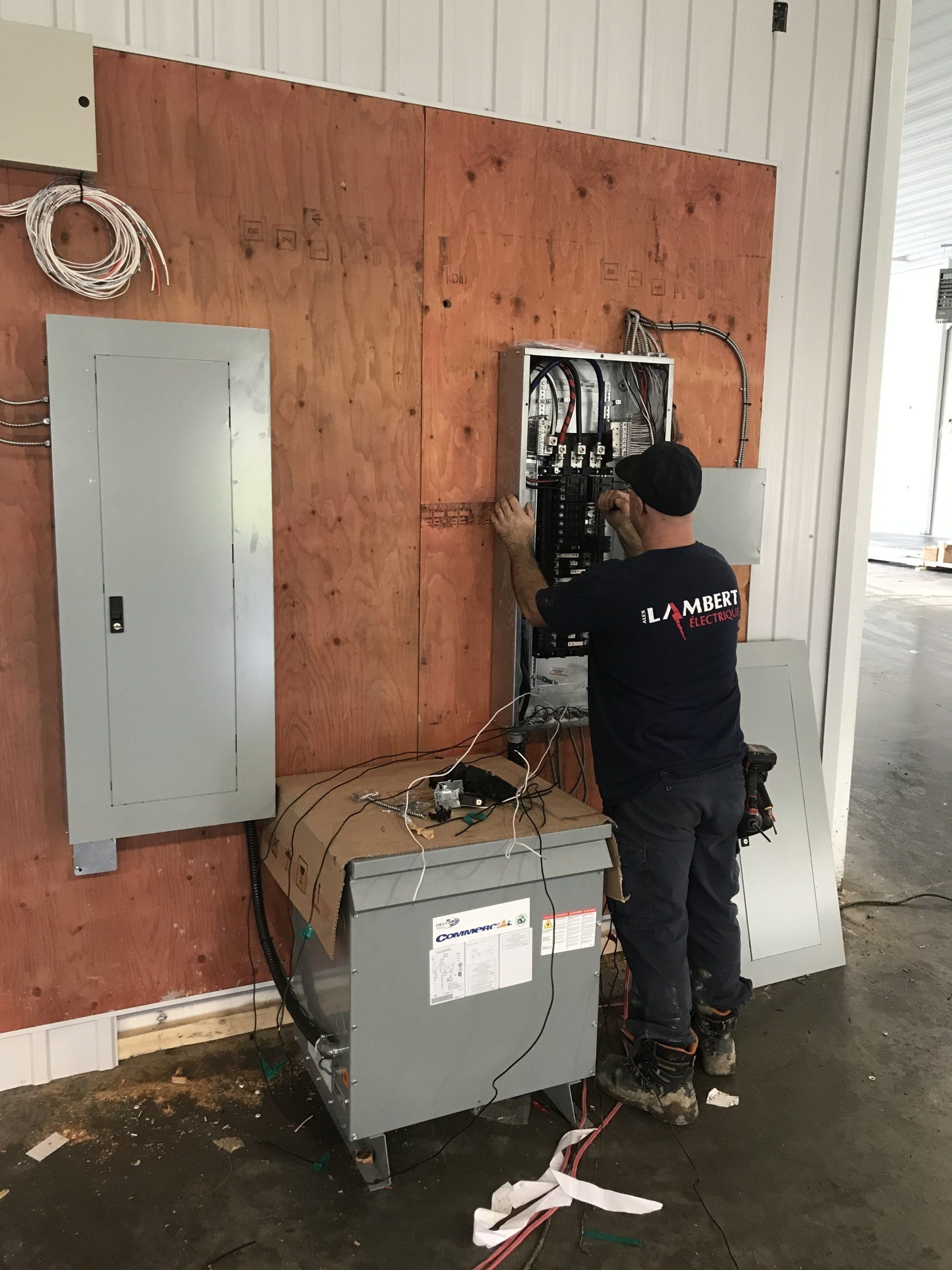 Électricien travaillant sur un panneau électrique, monté sur contreplaqué, avec transformateur sur roues dans un cadre commercial.