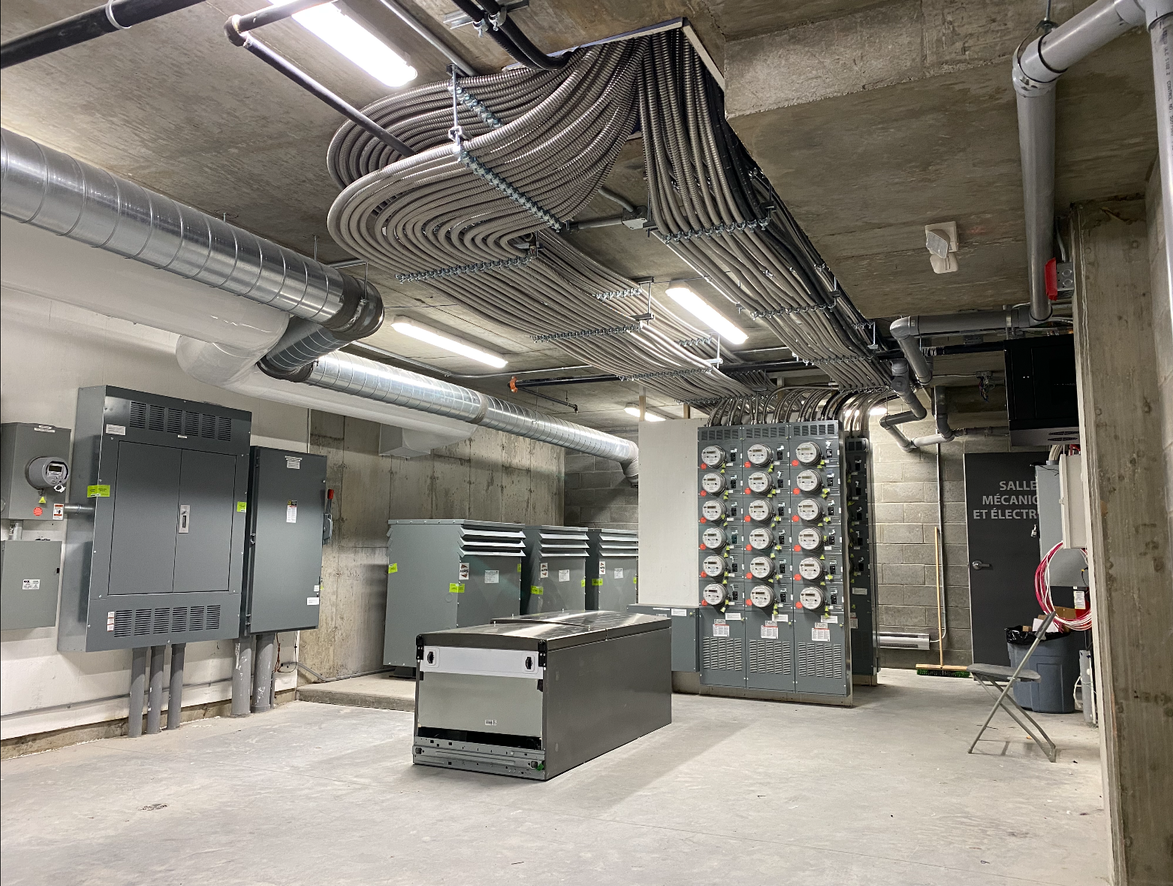Deux hommes travaillant sur un panneau électrique dans un environnement industriel ; l'un à genoux, l'autre debout.
