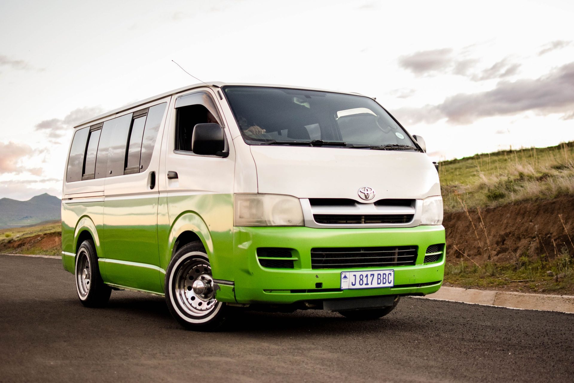 Green and white Toyota HiAce van parked outdoors on a rural road.