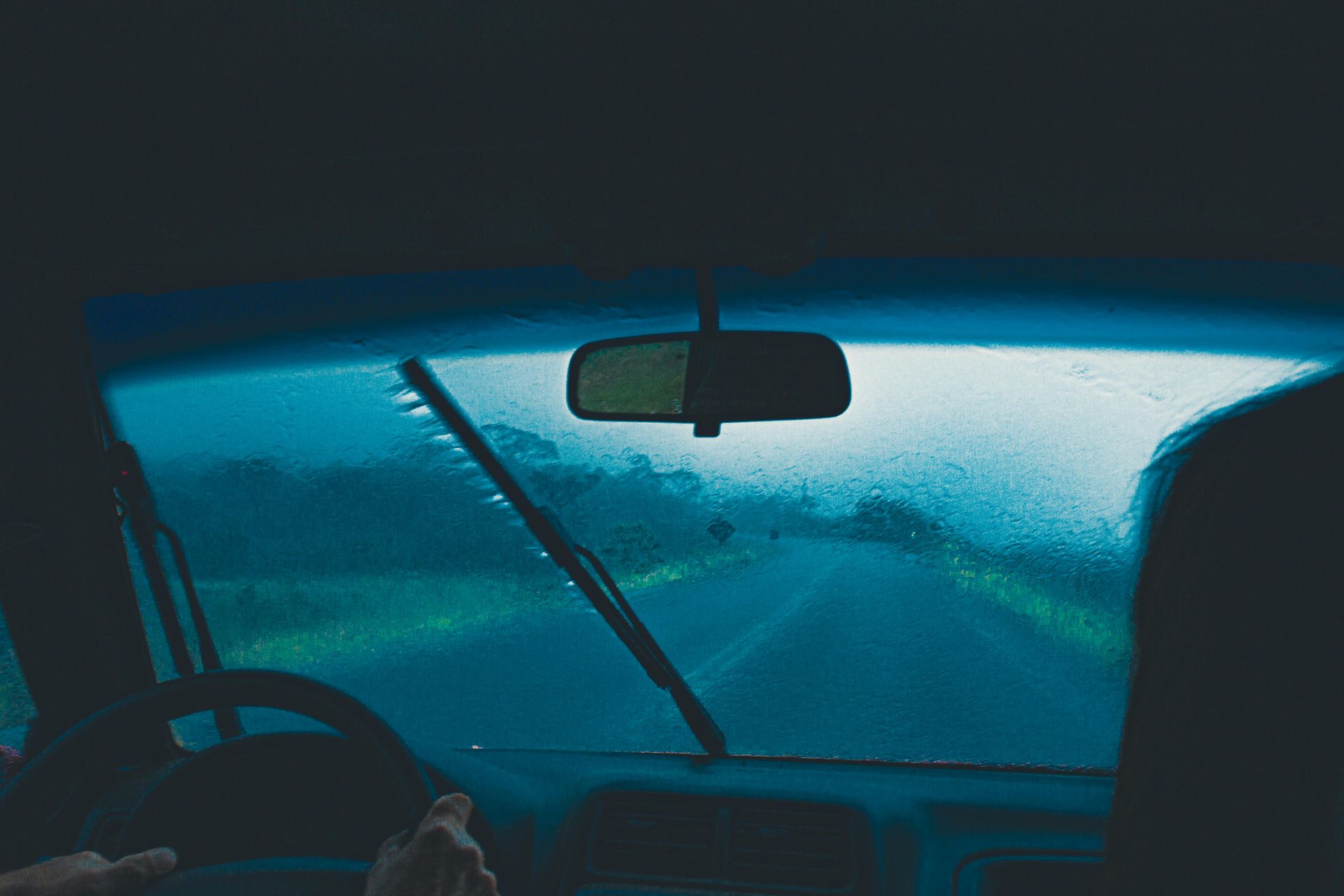 View from inside a car driving in heavy rain, windshield wipers clearing a blurred highway