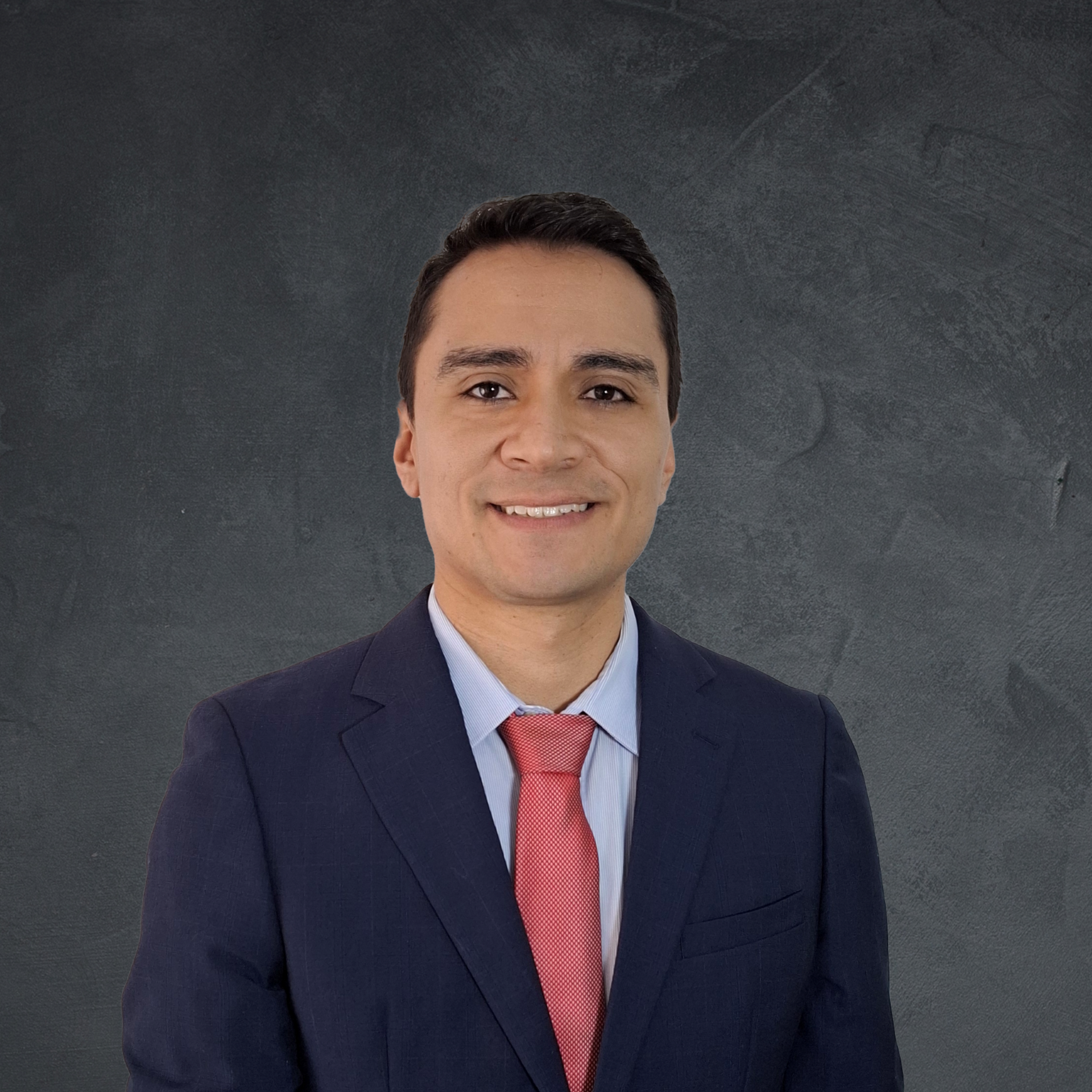 Man in suit, red tie, smiling against a dark background.