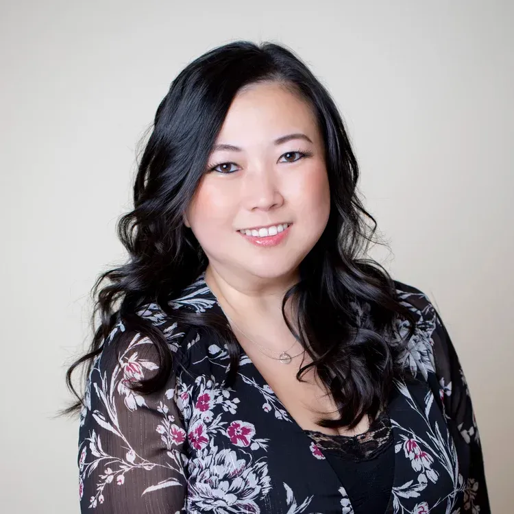 Woman with black hair smiles, wearing floral print jacket and black top. Light background.