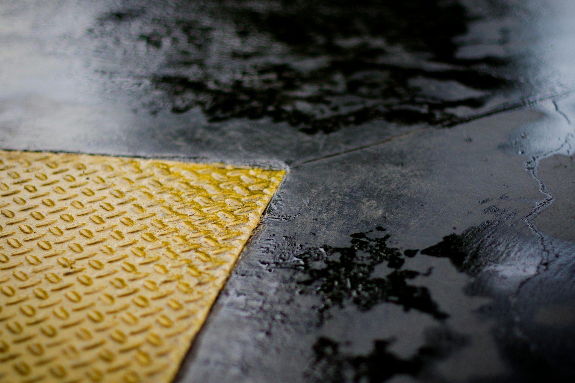 Yellow, diamond-plate corner meets wet, dark concrete floor.