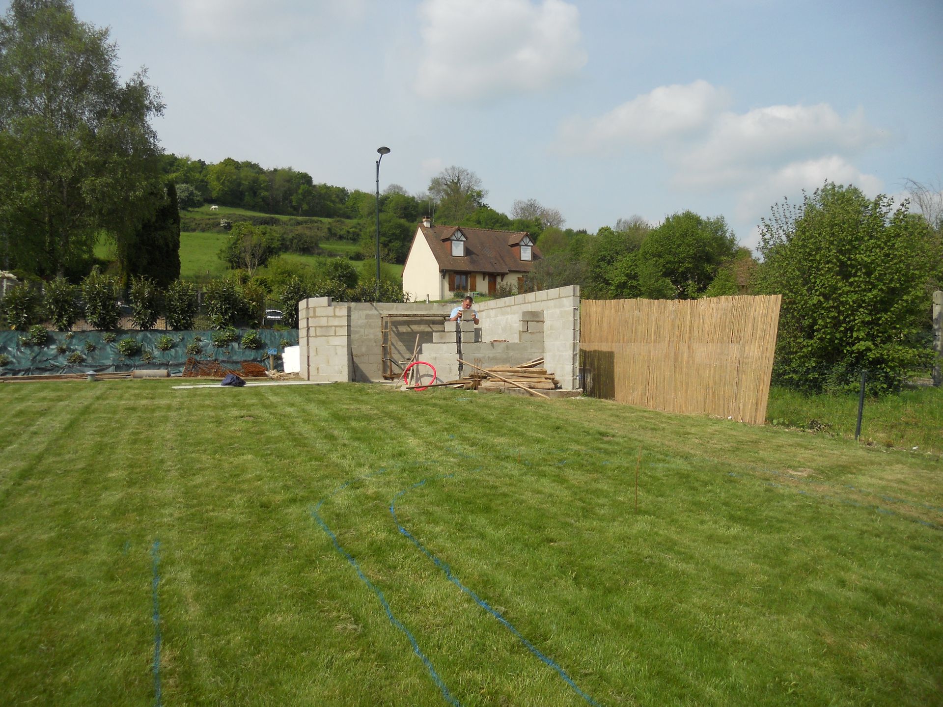 Cour herbeuse avec un petit abri de jardin blanc, des panneaux de clôture en bois, des arbres et une maison en arrière-plan.
