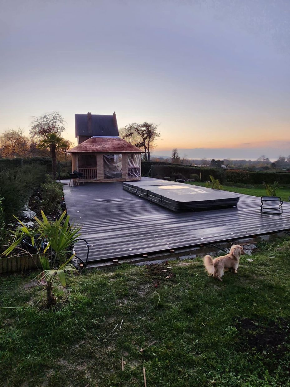 Vue du coucher de soleil sur une terrasse de jardin avec un jacuzzi, des marches et un petit chien sur la pelouse.