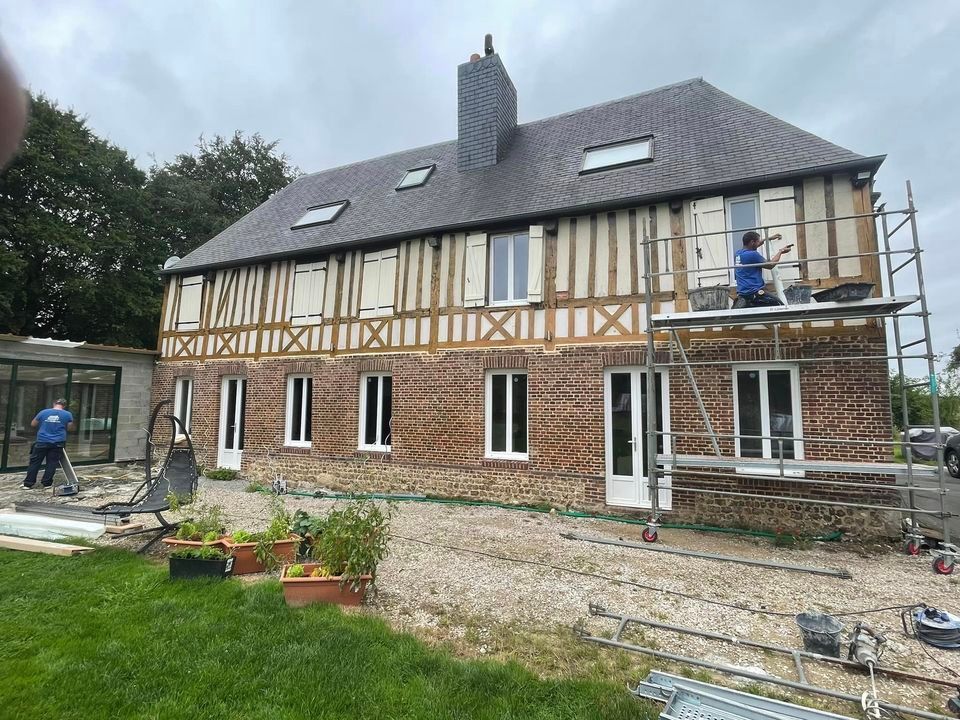 Maison en rénovation avec échafaudages et ouvriers dans une cour gazonnée