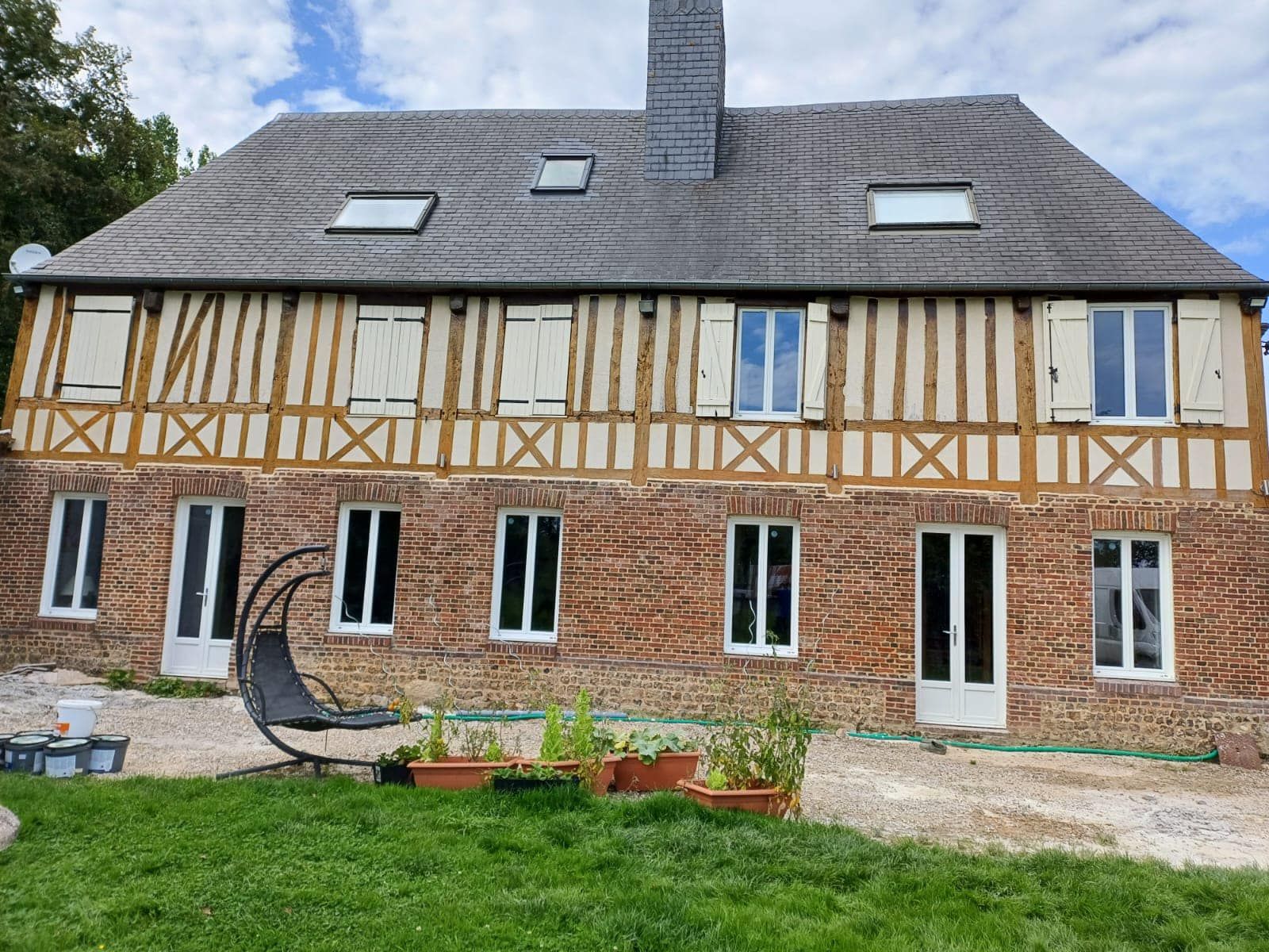 Maison en briques et à colombages avec toit gris, fenêtres blanches et petit jardin devant.
