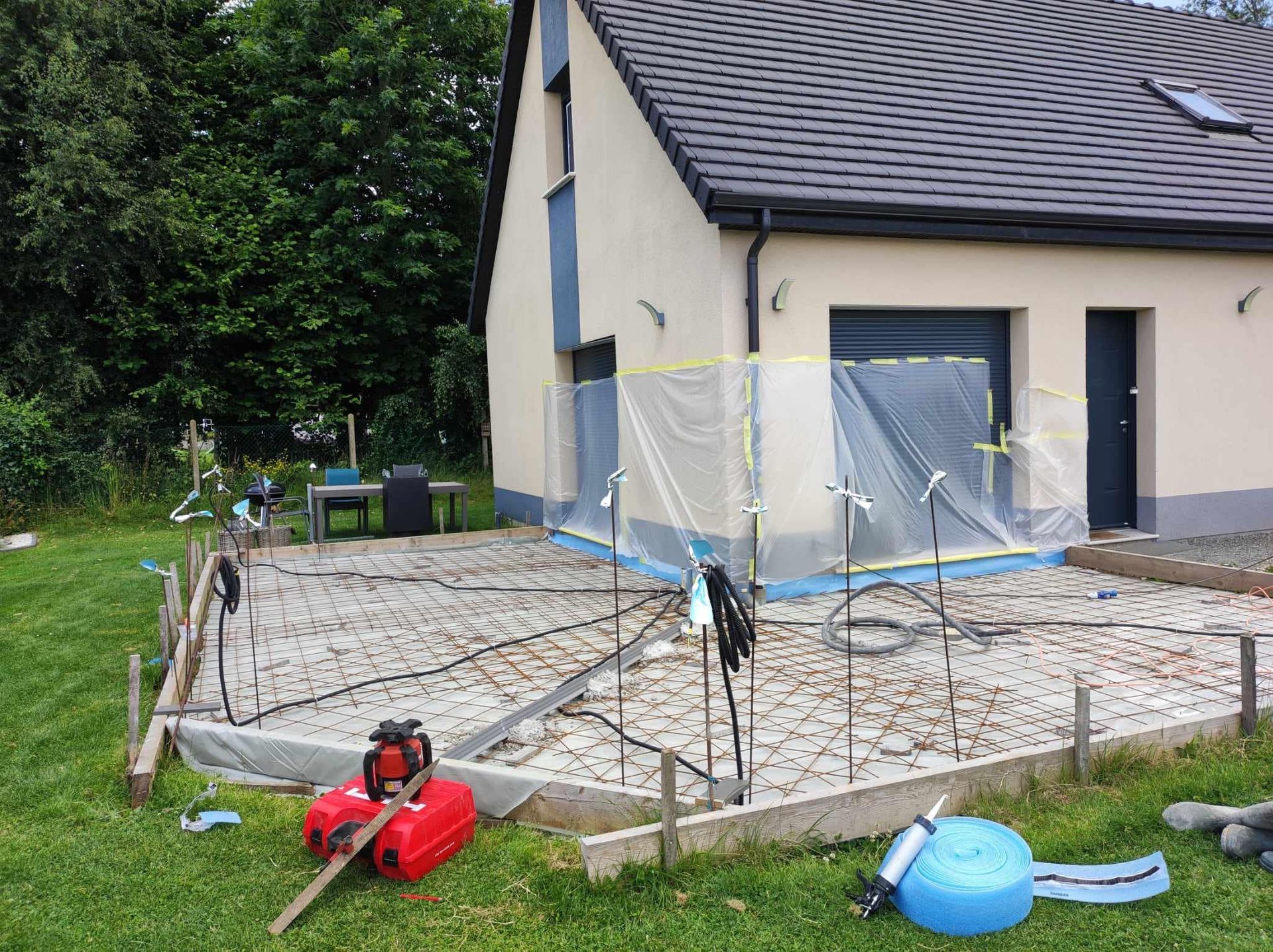 Terrasse de maison en construction avec des barrières de sécurité, des outils et des matériaux de construction éparpillés sur la pelouse