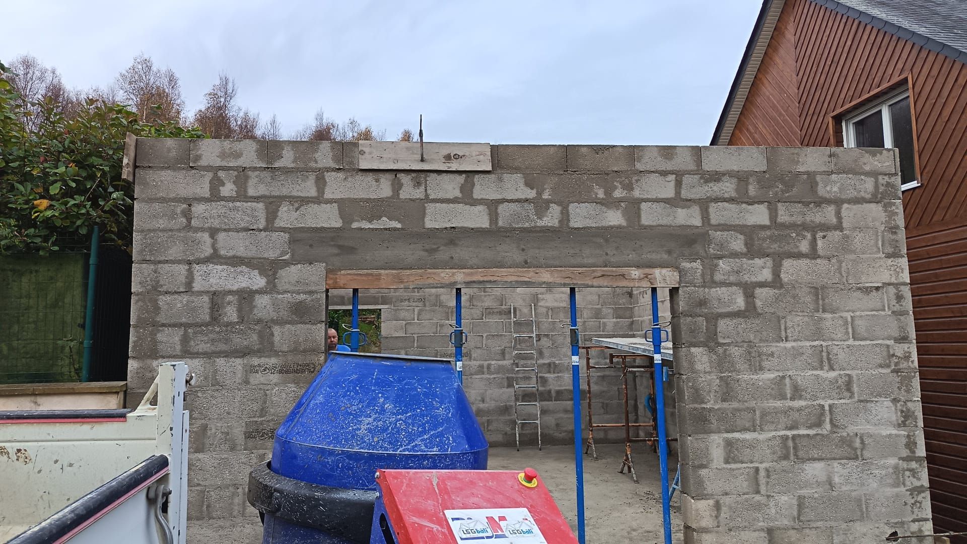 Mur en parpaings partiellement construit, avec échafaudages et matériaux de couverture, sur un chantier.