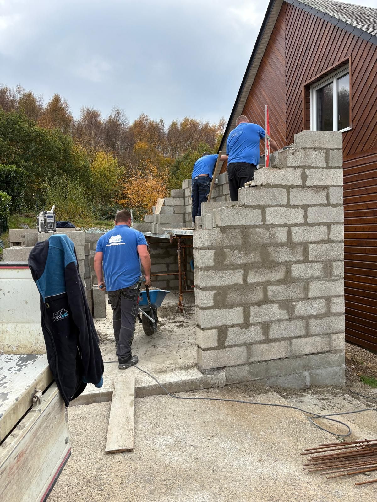 Des ouvriers construisent un mur en parpaings à côté d'une maison en briques sur un chantier extérieur