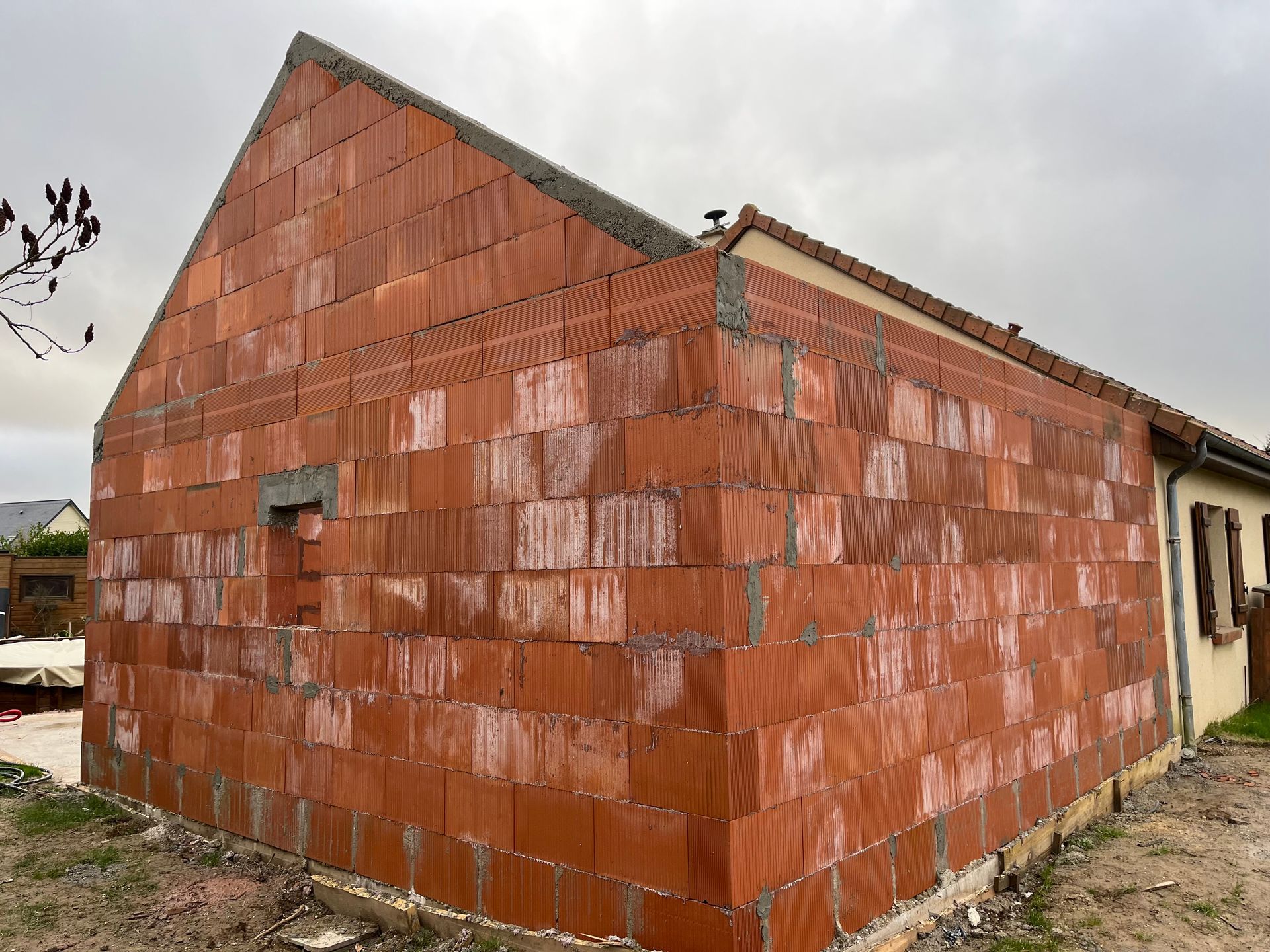 Maison en briques rouges partiellement construite, toit inachevé et ciel nuageux