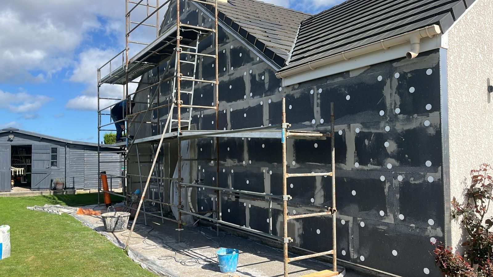 Maison en construction avec échafaudages et revêtement extérieur noir par une journée ensoleillée