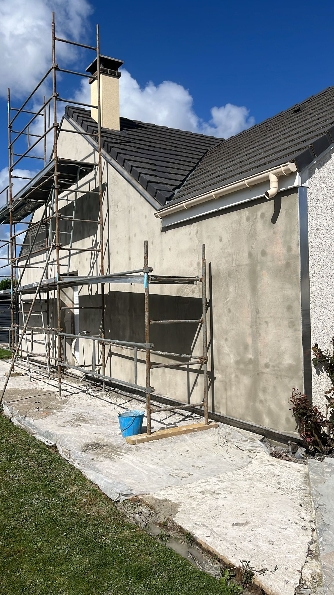 Extérieur de la maison avec échafaudages et crépi frais sous un ciel bleu