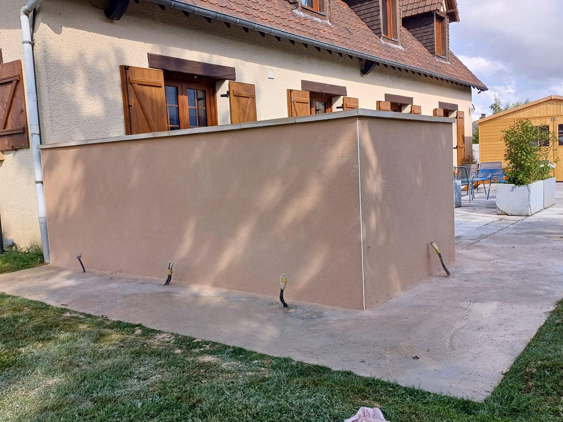 Extension en stuc beige attenante à une maison, avec toit plat et terrasse en béton dans une cour résidentielle.