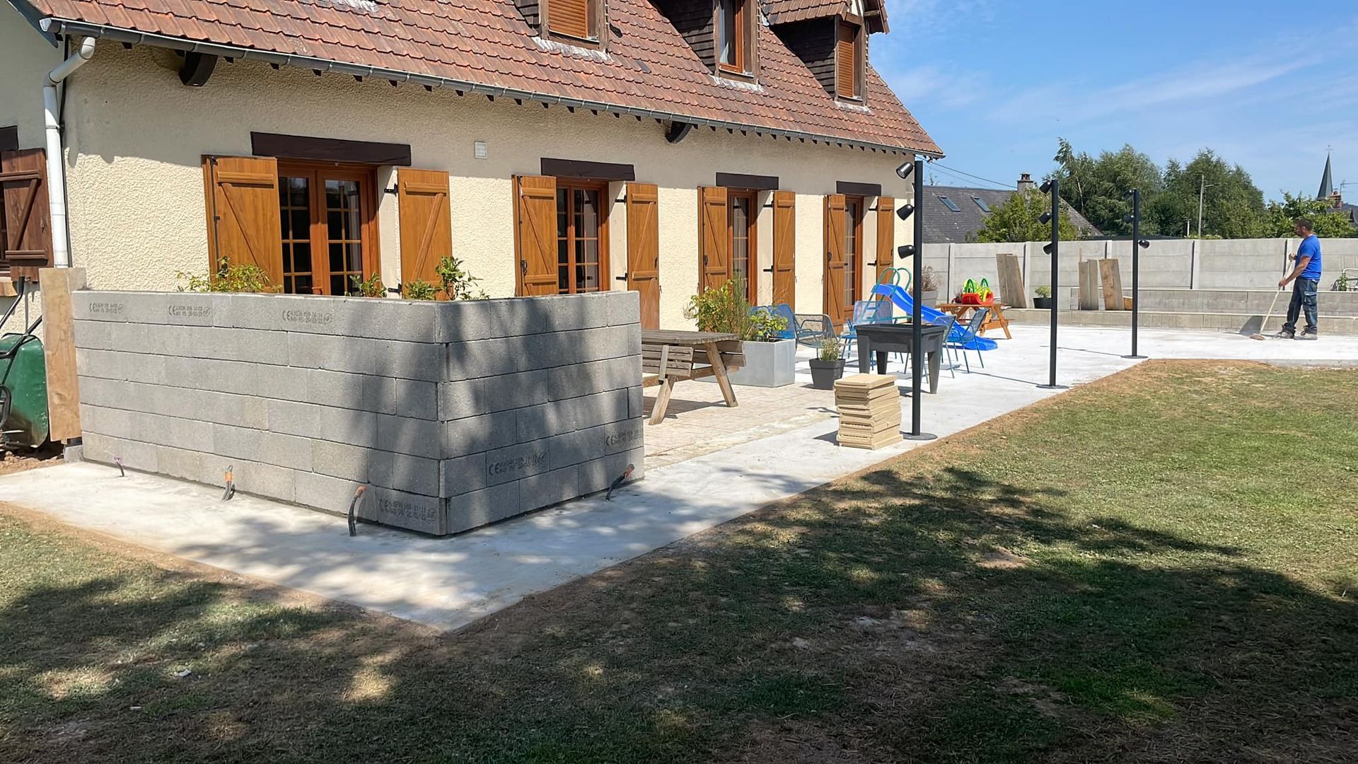 Terrasse arrière avec une maison en pierre, un muret en béton, des jeux d'extérieur bleus et une pelouse.