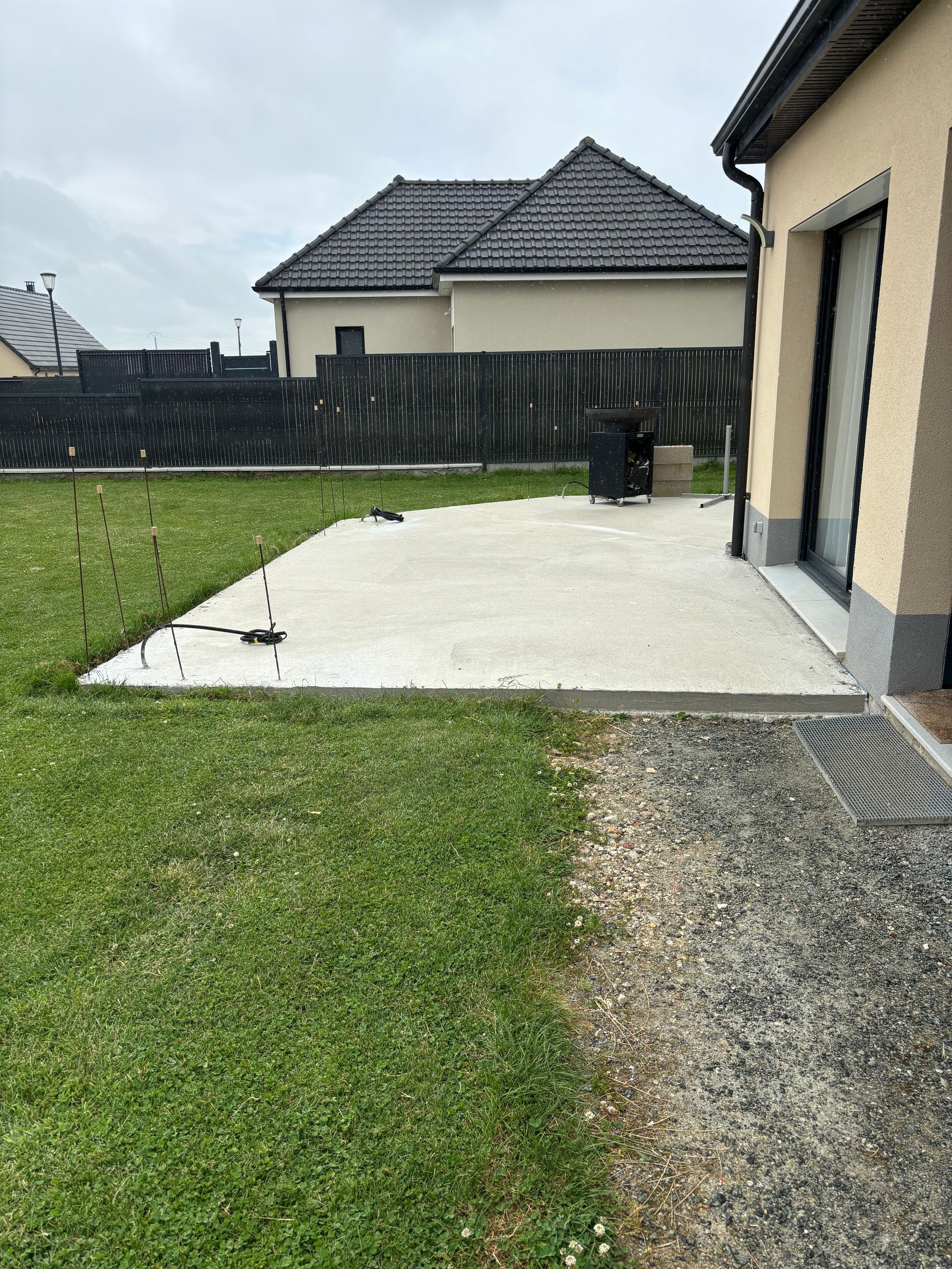 Terrasse arrière avec dalle de béton, pelouse, allée de gravier et maisons voisines