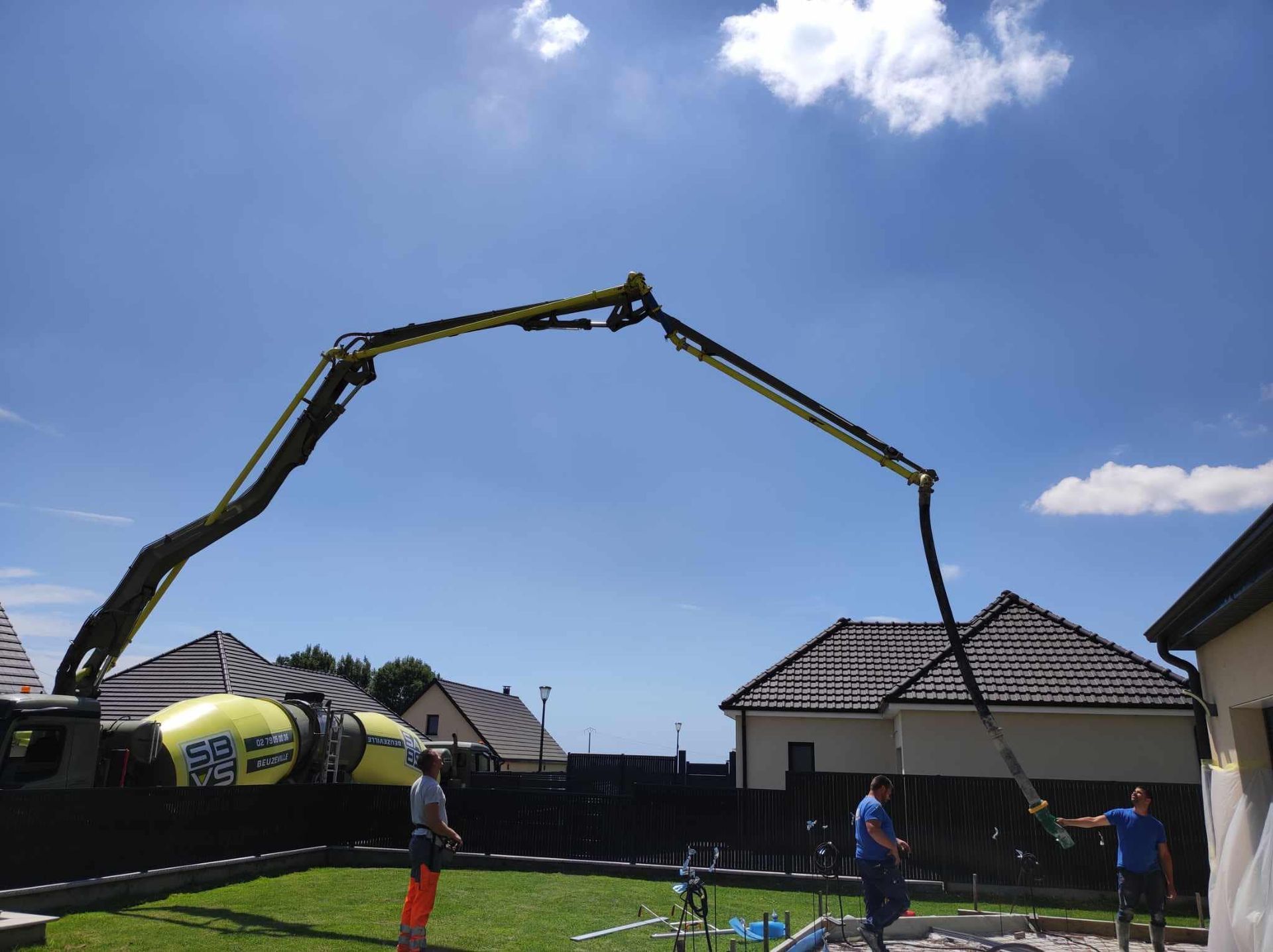 Bras d'une pompe à béton s'étendant au-dessus de maisons sur un chantier de construction par une journée ensoleillée