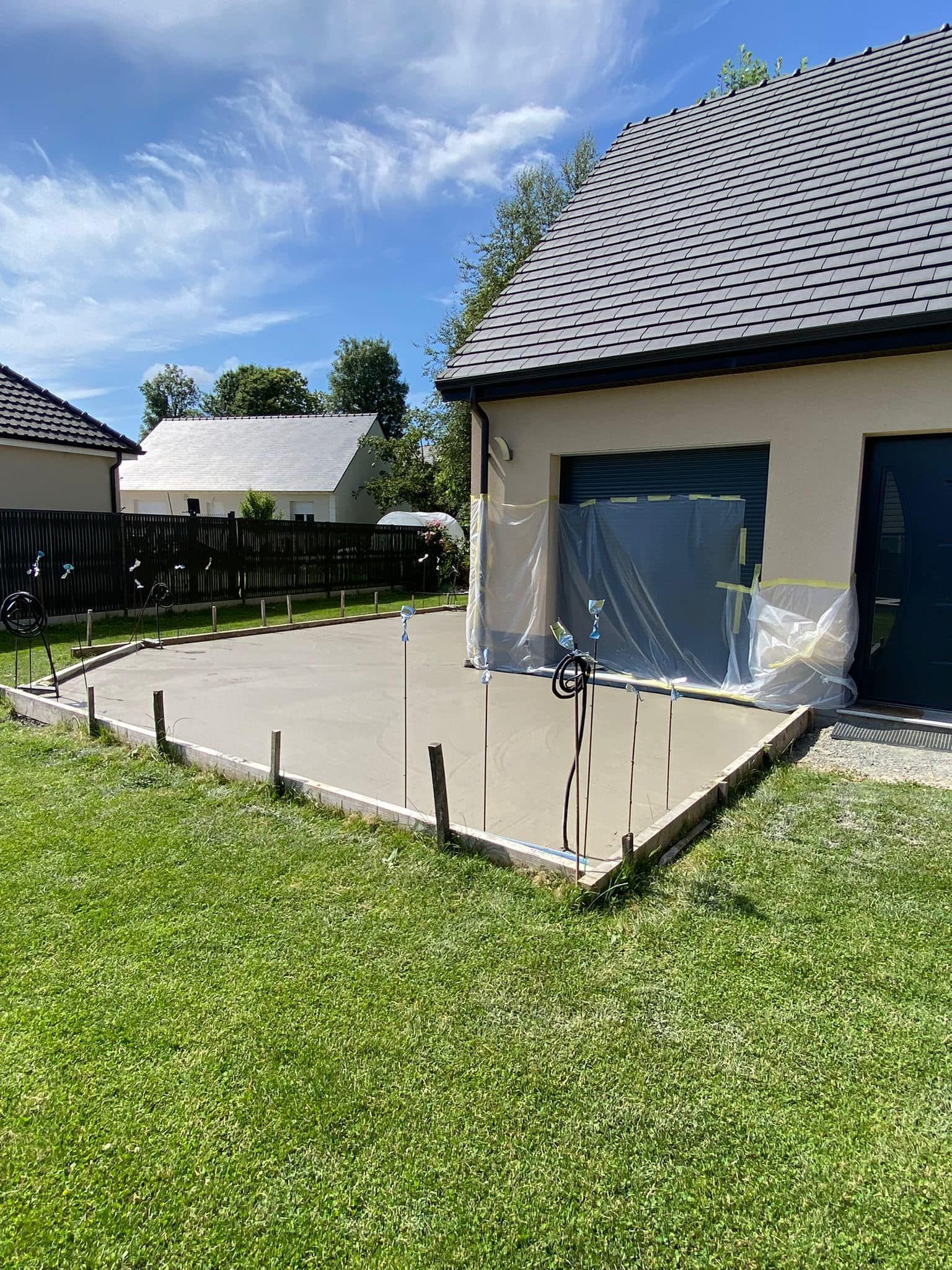 Terrasse arrière attenante à une maison au toit de tuiles, avec de la pelouse et un ciel d'un bleu éclatant.