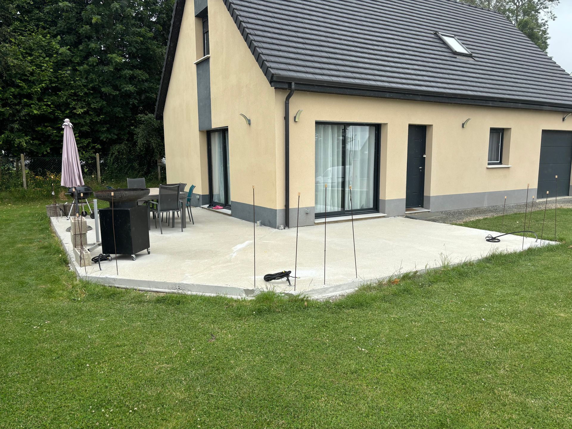 Maison moderne avec terrasse pavée, table et chaises d'extérieur et jardin gazonné